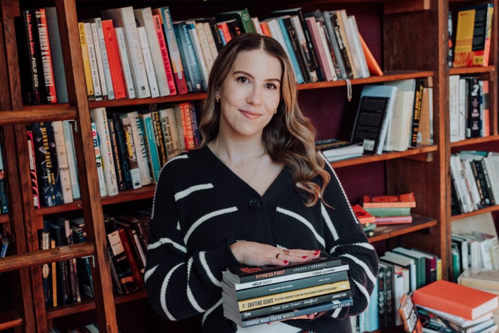 Ashlyn Anderson holds a stack of books from authors she's worked with; bookshelves are in the background